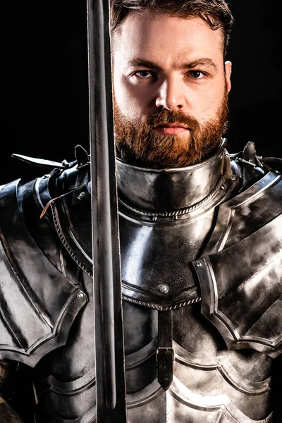Handsome knight in armor holding sword isolated on black — Stock Photo