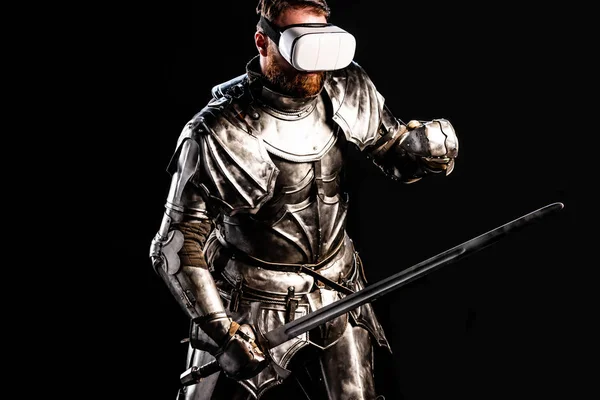 Лицар з гарнітурою віртуальної реальності в обладунках, що тримає меч і бореться ізольовано на чорному — стокове фото