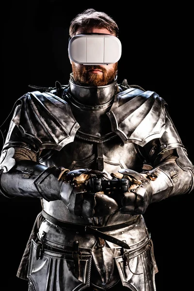 KYIV, UKRAINE - OCTOBER 9, 2019: knight with virtual reality headset in armor holding joystick on black background — Stock Photo