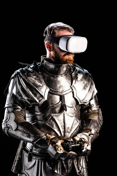 QUIIV, UCRÂNIA - OUTUBRO 9, 2019: cavaleiro com fone de ouvido de realidade virtual em armadura segurando joystick em fundo preto — Fotografia de Stock