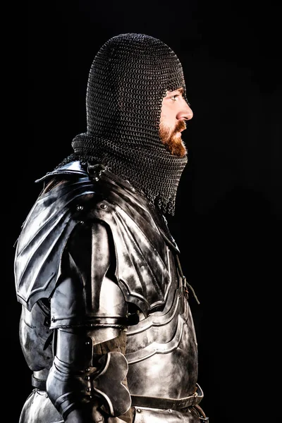 Vista lateral de belo cavaleiro em armadura isolado em preto — Fotografia de Stock