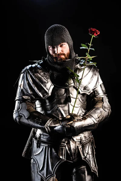 Bonito cavaleiro em armadura segurando rosa isolado no preto — Fotografia de Stock