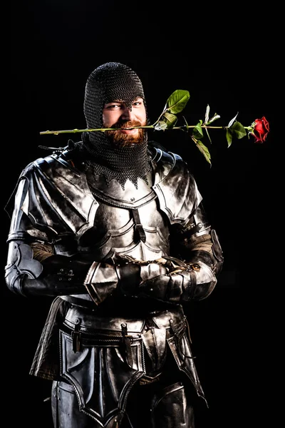 Bonito cavaleiro em armadura segurando rosa isolado no preto — Fotografia de Stock
