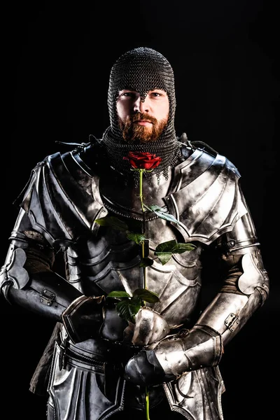 Handsome knight in armor holding rose isolated on black — Stock Photo