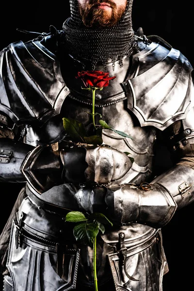 Cropped view of knight in armor holding rose isolated on black — Stock Photo