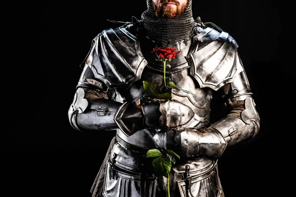 Cropped view of knight in armor holding rose isolated on black — Stock Photo