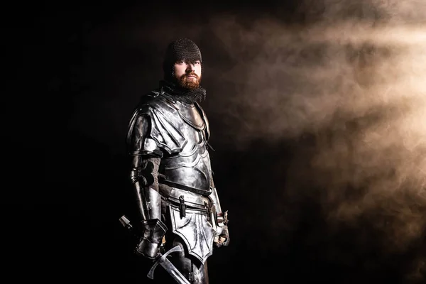 Bel cavaliere in armatura che tiene la spada su sfondo nero — Foto stock