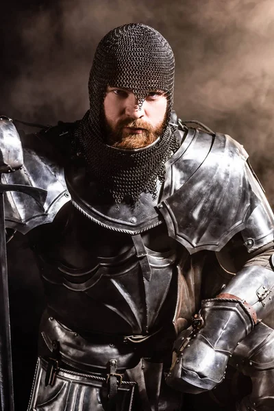Handsome knight in armor holding sword on black background — Stock Photo