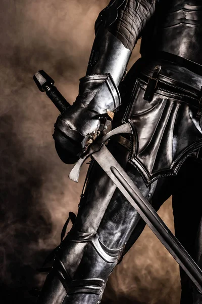 Cropped view of knight in armor holding sword on black background — Stock Photo