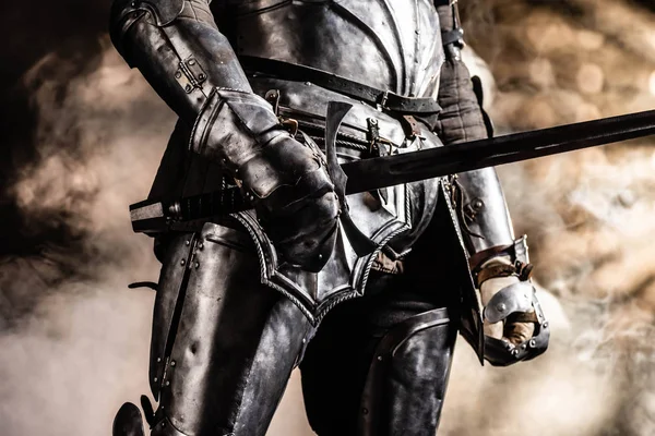 Cropped view of knight in armor holding sword on black background — Stock Photo