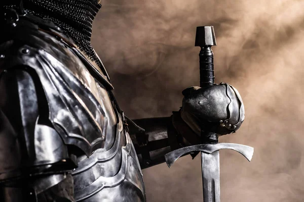Vista recortada de caballero en armadura sosteniendo espada sobre fondo negro - foto de stock