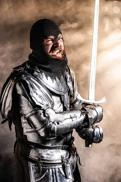 Bonito cavaleiro em armadura segurando espada e lutando no fundo preto — Fotografia de Stock