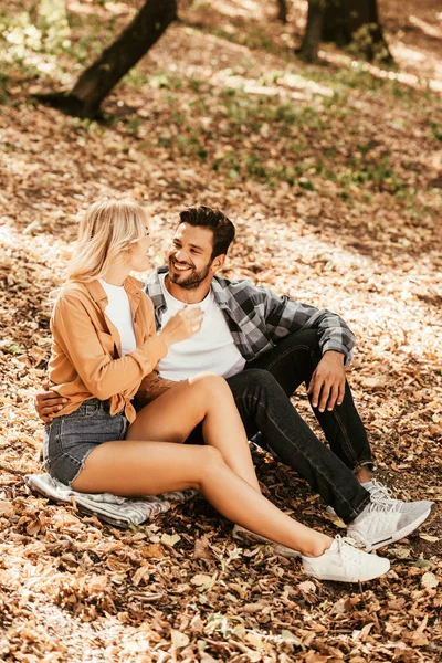 Felice giovane coppia che si guarda mentre si siede sul fogliame autunnale nel parco — Foto stock