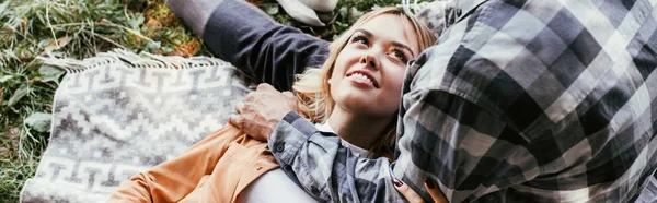 Cropped view of man embracing smiling girlfriend lying on blanket in park, panoramic shot — Stock Photo