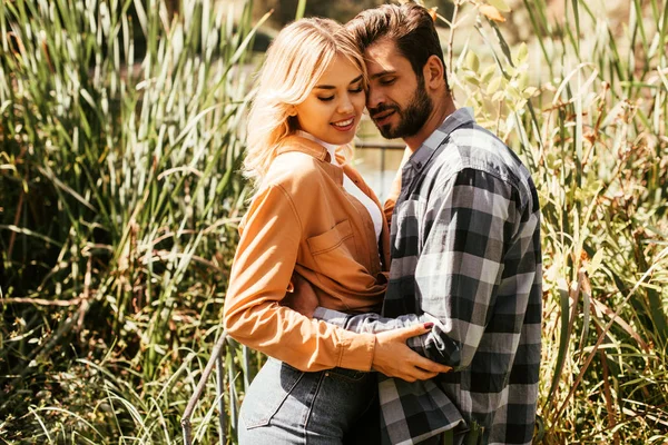 Feliz, hermosa chica y guapo joven abrazando en matorral de junco - foto de stock