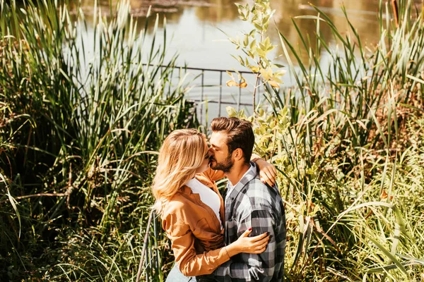 Feliz joven pareja abrazando y abrazando en matorral de junco cerca del lago - foto de stock