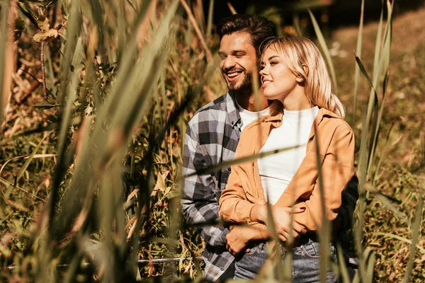Selective focus of happy young man embracing smiling girlfriend in thicket of sedge — Stock Photo