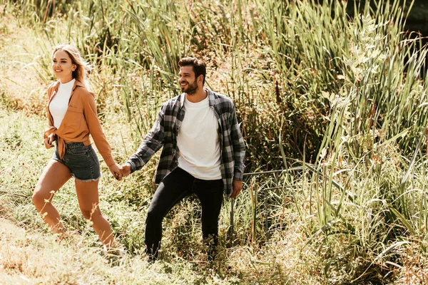 Alegre pareja joven cogida de la mano mientras camina en matorral de junco - foto de stock