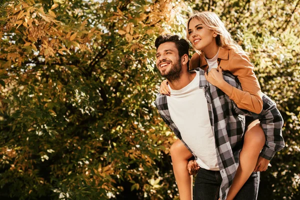 Feliz joven piggybacking novia feliz en el parque - foto de stock