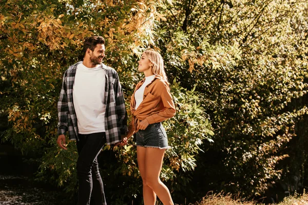 Young, happy couple holding hands and looking at each other while walking in park — Stock Photo