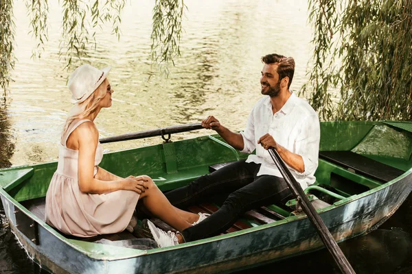 Mujer joven en vestido de sol con novio feliz sentado en barco en el lago - foto de stock