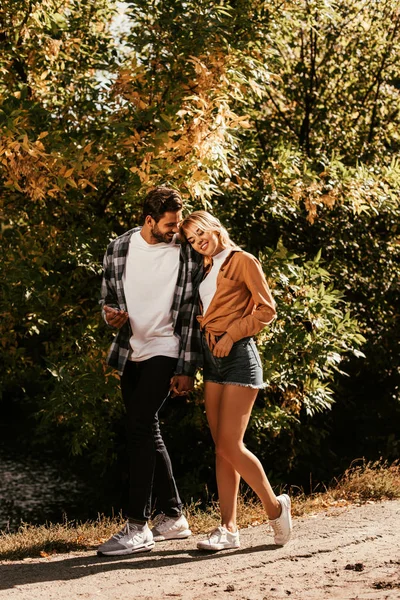 Happy young woman leaning on shoulder of boyfriend while walking in park — Stock Photo