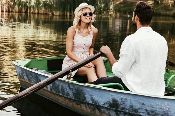 Sorridente ragazza in sundress e occhiali da sole guardando fidanzato in barca — Foto stock