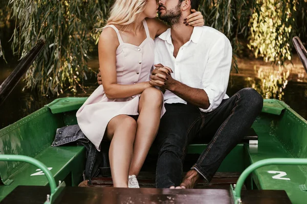 Обрізаний вид щасливої молодої пари цілується, сидячи в човні на озері — стокове фото