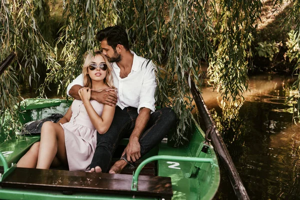 Bel homme embrassant petit ami attrayant tout en étant assis dans le bateau sur le lac — Photo de stock