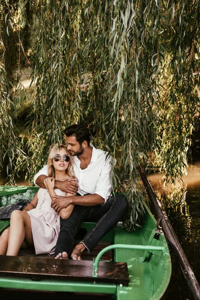 Handsome man hugging attractive boyfriend while sitting in boat on lake — Stock Photo