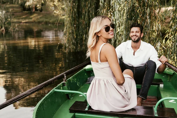 Fröhliche junge Frau blickt in die Kamera, während sie im Boot neben ihrem glücklichen Freund sitzt — Stockfoto