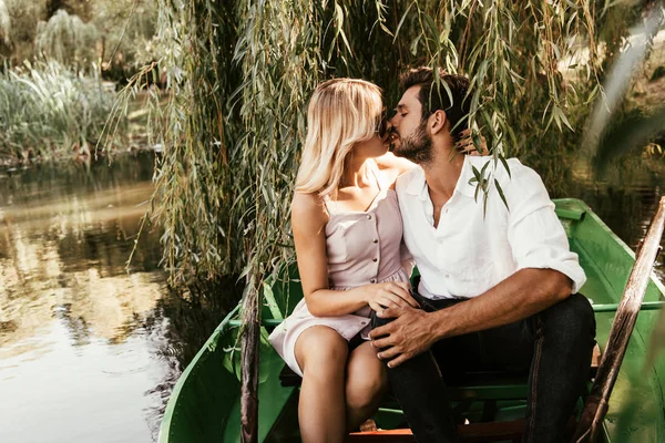 Happy young couple kissing while sitting in boat on lake — Stock Photo