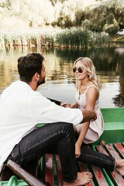 Atractiva, mujer sonriente mirando novio mientras está sentado en barco en el lago - foto de stock