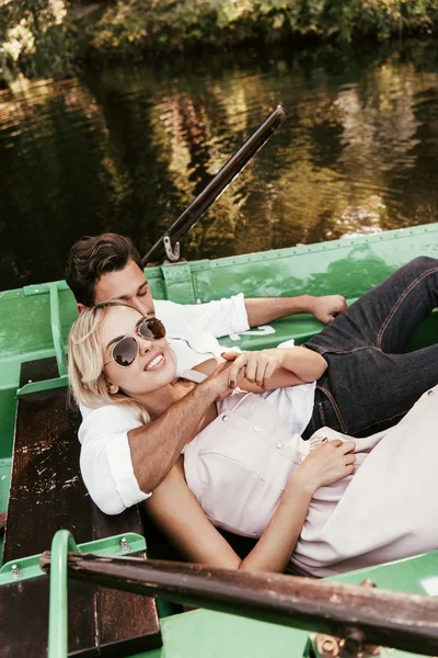 Молодой человек обнимает веселую девушку, пока лежит в лодке на озере — стоковое фото