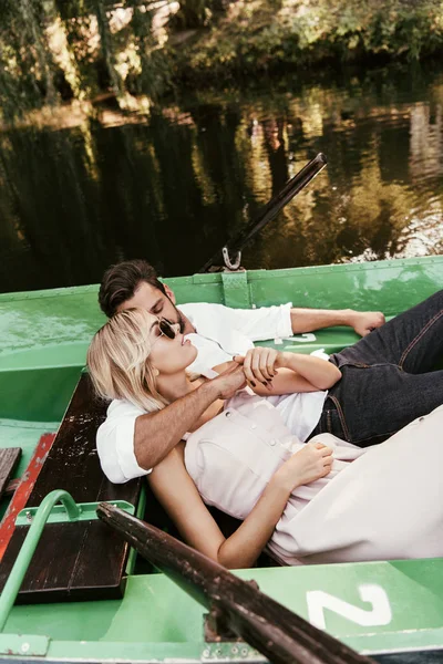Jovem abraçando namorada atraente enquanto deitado em barco no lago — Fotografia de Stock