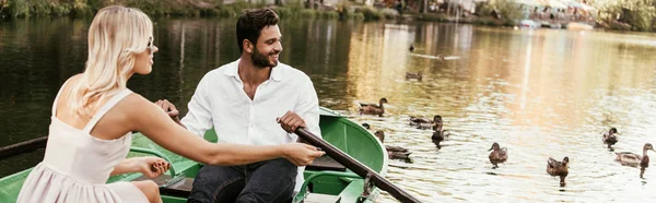 Panoramic shot of young couple in boat on lake near flock of ducks — Stock Photo