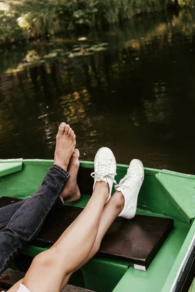 Обрізаний вид на босоніж чоловіка і дівчину в кросівках, що розслабляються на човні на озері — стокове фото