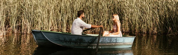 Colpo panoramico di coppia giovane in barca su fiume vicino a boscaglia di carice — Foto stock