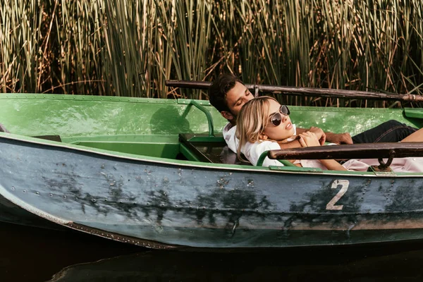 Pareja joven relajarse en barco en el río cerca de matorral de junco - foto de stock