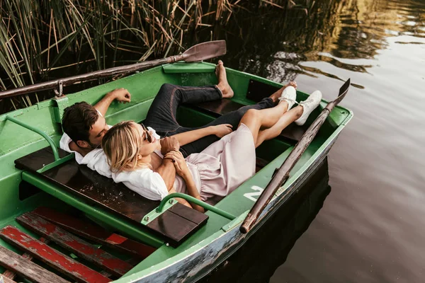 Feliz pareja joven relajarse en barco en el lago cerca de matorral de junco - foto de stock