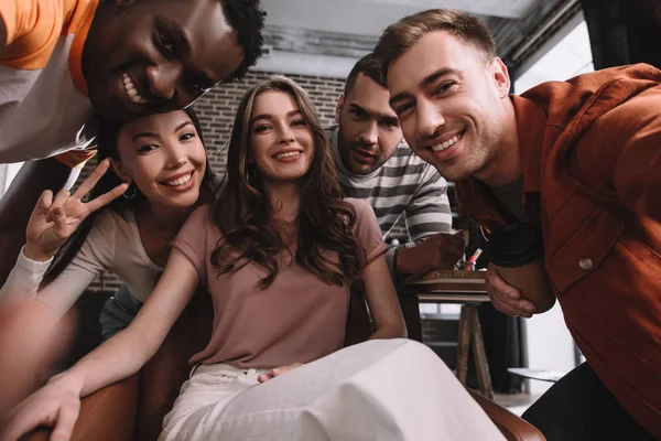 Junge, fröhliche multikulturelle Geschäftsleute, die im Büro in die Kamera lächeln — Stockfoto