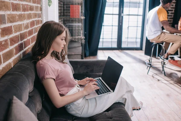 Young, thoughtful businesswoman using laptop while sitting on sofa in office — Stock Photo