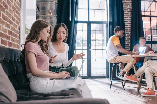 Joven mujer de negocios hablando con colega sentado en el sofá y el uso de la computadora portátil — Stock Photo