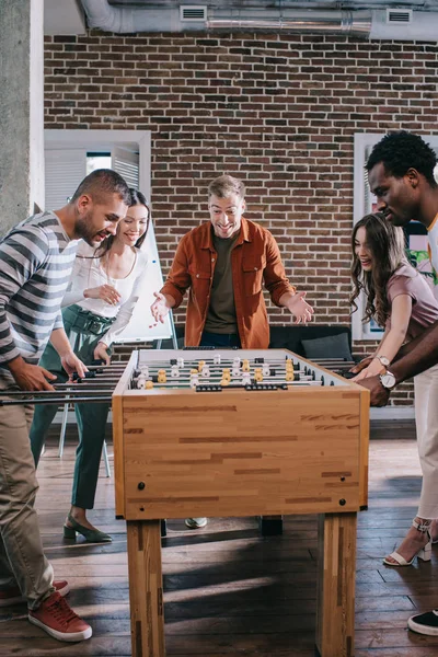 Alegres empresarios multiculturales jugando al futbolín en la oficina - foto de stock