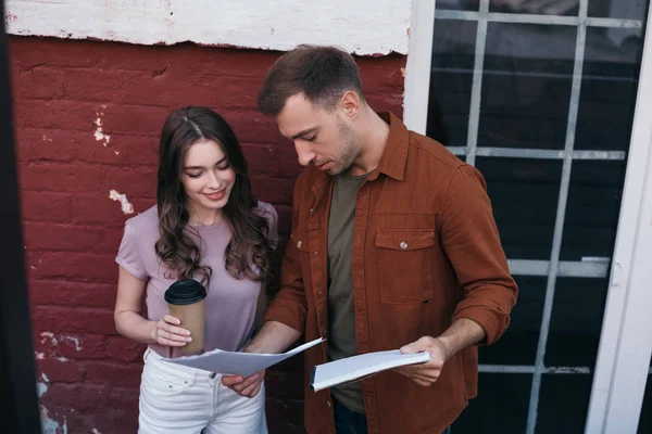 Empresário pensativo mostrando documentos para colega sorrindo segurando café para ir — Fotografia de Stock