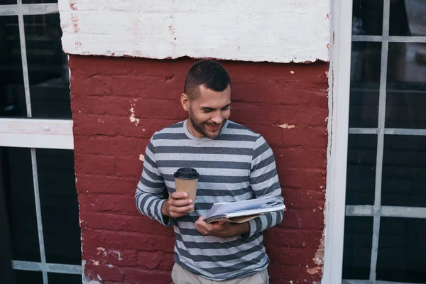 Joven hombre de negocios alegre leyendo documentos mientras sostiene el café para ir - foto de stock
