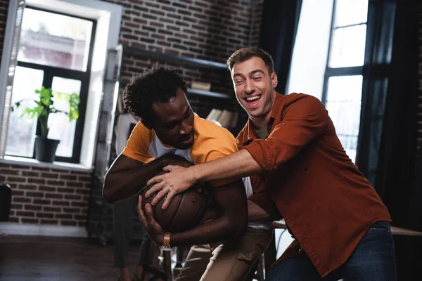 Junger, fröhlicher Geschäftsmann nimmt Basketball aus den Händen eines afrikanisch-amerikanischen Kollegen — Stockfoto