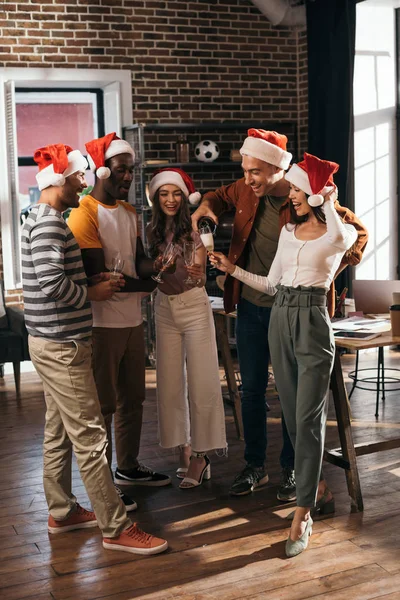 Glückliche multikulturelle Geschäftsleute mit Weihnachtsmannhüten, die im Büro Sektgläser klirren — Stockfoto