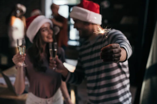 Selective focus of happy businessman and businesswoman in santa hats looking at each other while holding champagne glasses — Stock Photo