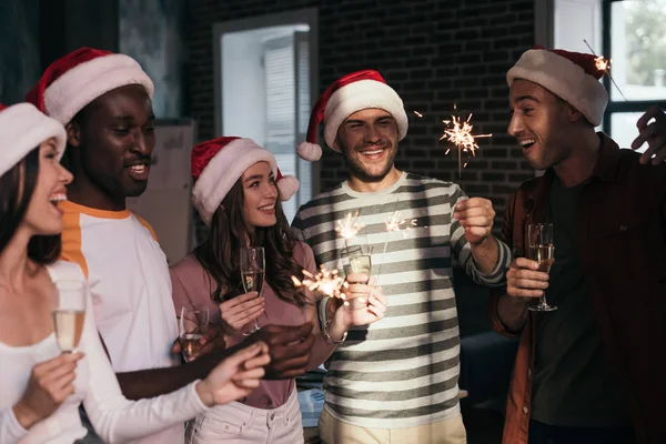 Heureux, jeunes gens d'affaires dans chapeaux Santa tenant des étincelles et des verres de champagne — Photo de stock